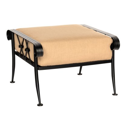 The Derby Ottoman is a square stool with a beige cushion on a black metal frame, featuring ornate curved armrests, a decorative X-pattern on the sides, and standing on four slender, curved legs.