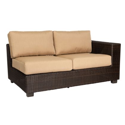 The Montecito Right Arm Facing Love Seat Sectional features a dark brown wicker frame with beige cushions, including two seat and two backrest cushions, and one right-side armrest. Its simple design is perfect for both indoor and outdoor settings.
