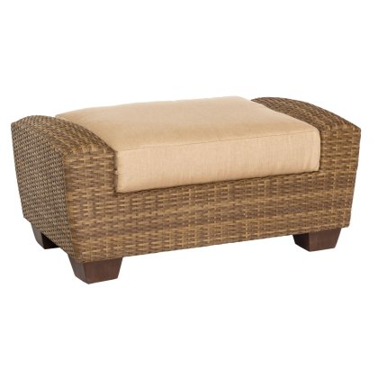 The Saddleback Ottoman is a rectangular wicker piece with a beige cushion, featuring a woven texture and sturdy wooden legs.