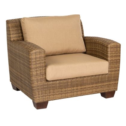 The Saddleback Lounge Chair features a boxy, modern design with wicker armrests, beige cushions, and wooden legs. Its textured brown and tan woven pattern offers a cozy and inviting seating option.