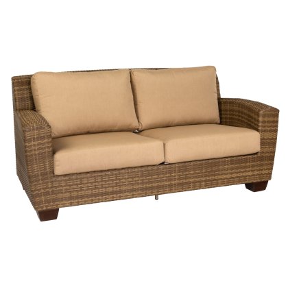 The Saddleback Love Seat is a brown wicker sofa with beige cushions, featuring wide armrests and two large back cushions for comfort. Its contemporary style makes it ideal for indoor or outdoor use.