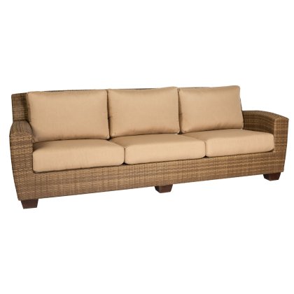 The Saddleback Sofa is a brown woven rattan piece with three beige cushioned seats and backrests, featuring short, dark wooden legs with a simple, contemporary design.