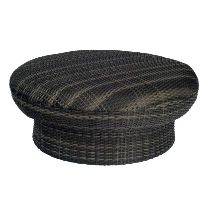 The Genie Ottoman Coffee Table is a round, woven wicker piece with a textured surface, featuring a dark finish. It has a thick cylindrical base supporting the circular top.