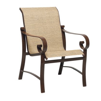 The Belden Sling Dining Armchair features a wooden frame with curved armrests, a light beige woven fabric seat and backrest, a slightly reclined design, and elegant scroll details on the arms.