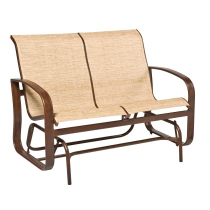 The Cayman Isle Sling Gliding Love Seat is a two-seat outdoor glider with a brown metal frame and tan fabric seats, featuring curved armrests and a seamless design, perfect for patios or gardens.